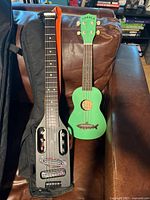Traveler Guitar Ultra-Light Acoustic and Makala green ukulele resting on sofa with gig bag