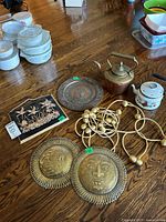 Group shot of all items on floor: plaque, metal plates, copper kettle, enamel kettle, curtain cords