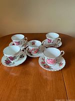 Five teacup and saucer sets displayed on wooden surface