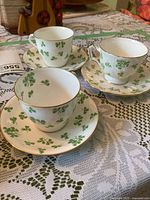 Three Aynsley shamrock teacups on matching saucers set on lace tablecloth
