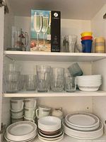 Cabinet shelves with Libbey boxed flutes, glass tumblers, pitcher, plastic cups, Corelle Woodland plates and mugs