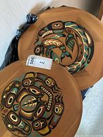 two carved wood discs showing painted Indigenous imagery