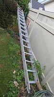Full view of aluminum extension ladder leaning against fence