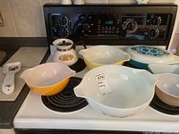 All items on stove: four Pyrex bowls, Pyrex divided casserole with lid, Pyrex fridge dish, Corning Ware sauce pot