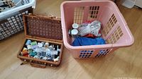 Overall view of wicker sewing basket and pink laundry basket on floor