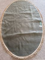Full view of oval sage green rug with fringe