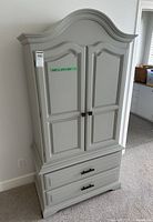 Front view of gray armoire with doors closed and drawers visible