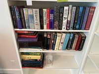 Three shelves of assorted hardcover books and one horse-head bookend visible