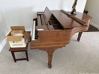 Side view of baby grand piano, small stool with box of sheet music visible