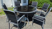 Round black glass patio table with six chairs arranged around it
