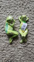 Two green ceramic frog figurines side by side on carpet