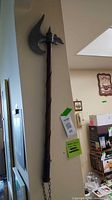 Full view of 31" Denex battle axe hanging on wall showing entire length, chain and leather wraps