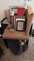 Chair holding stack of assorted frames, metal stands, pad, grey bag below