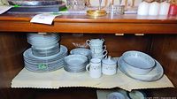 Cabinet shelf with stacked dinner plates, side plates, bowls, platter, serving bowl, creamer and sugar bowl