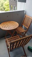 Round wood folding table and two matching folding chairs on balcony