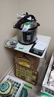 Geek Chef pressure cooker on white plastic table with scale and box below