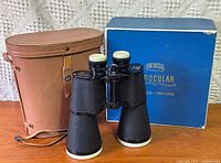 Binoculars standing with leather case and box visible