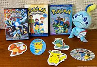 Group shot of three Pokemon DVDs, Sobble plush and six stickers