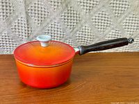 Side view showing orange enamel body, lid, wooden handle