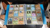 Binder open on chair displaying two pages of Pokémon cards (24 cards visible)