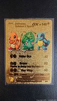 Front of gold metal GX card with Charmander, Bulbasaur, Squirtle and stats