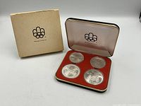 Display case open with four coins and outer sleeve