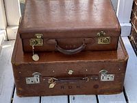 Two stacked brown leather luggage pieces showing size difference and hardware