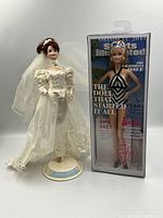Both Barbie dolls side by side, boxed Sports Illustrated Barbie and dressed Bridal Barbie on stand
