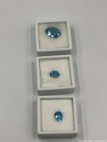 Three light blue faceted gemstones in display boxes