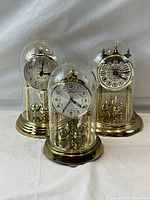 Front view of all three brass German anniversary clocks under glass domes