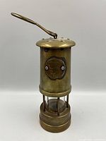 Front view of brass miner's lamp showing medallion, glass chimney and bars