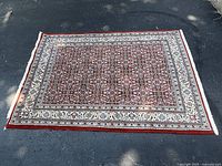 Full view of red and ivory patterned rectangular rug on asphalt