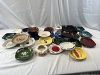 All thirty ashtrays and change dishes grouped on cloth backdrop