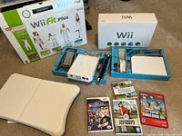 Full lot showing two Wii consoles in trays with accessories, Balance Board, five game cases, Wii Fit Plus and console boxes