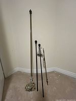 Three curtain rod sets with finials, rods, rings and hardware displayed upright against wall