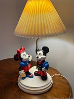 Full view of lamp with figurine base, pleated shade and cord visible