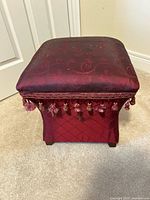 Full view of stool front showing upholstery, tassels, wood feet