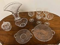 All pieces on tabletop: vase, lidded dish with spoon, candy dish, two plates, five wine glasses