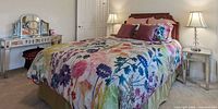 Bed made with floral duvet cover, matching shams, green bed skirt, dusty rose and plum decorative pillows