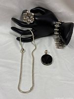 Group shot of ring, necklace, pendant, bracelet displayed on black hand stand