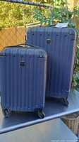 Both navy blue hard-shell suitcases side by side showing size difference, wheels, and handles