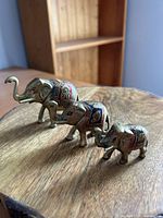 Three brass elephants on wooden surface showing painted details and graduated sizes