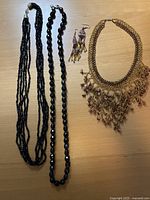 All four jewellery pieces laid out: two black bead necklaces, goldtone stone fringe choker, beaded earrings