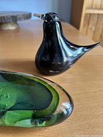 Black glass bird figurine front left, part of green paperweight visible