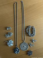 All nine silver-tone jewellery pieces laid out: six brooches, bracelet, two pendant necklaces