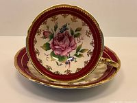 Interior of teacup resting on saucer showing rose motif, cranberry border and gilt detail