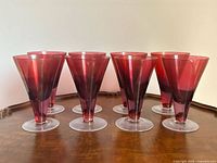 Set of eight ruby red conical footed glasses on wood surface