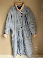 Full front view of long sky blue Skila parka hanging on wall