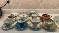 All twelve tea cup and saucer sets arranged on counter