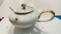 Full left side view of teapot showing gold-trimmed handle and starburst motif